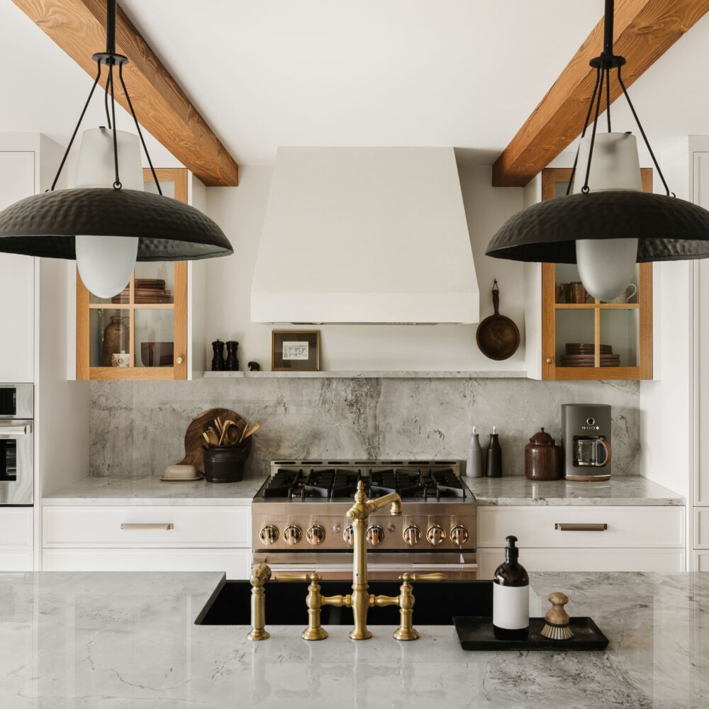 Custom kitchen by Alderstone Homes featuring natural wood beams, marble countertops, and modern brass fixtures.