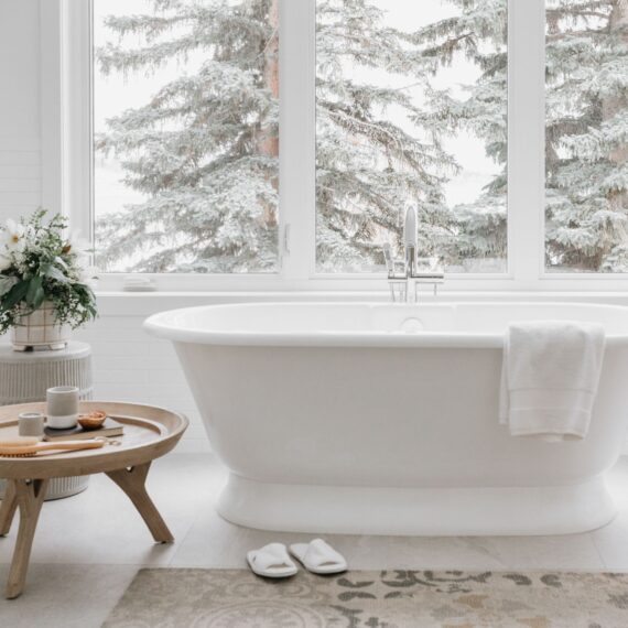 Freestanding bathtub with large windows overlooking winter forest, designed by Alderstone Homes for a serene bathroom retreat.