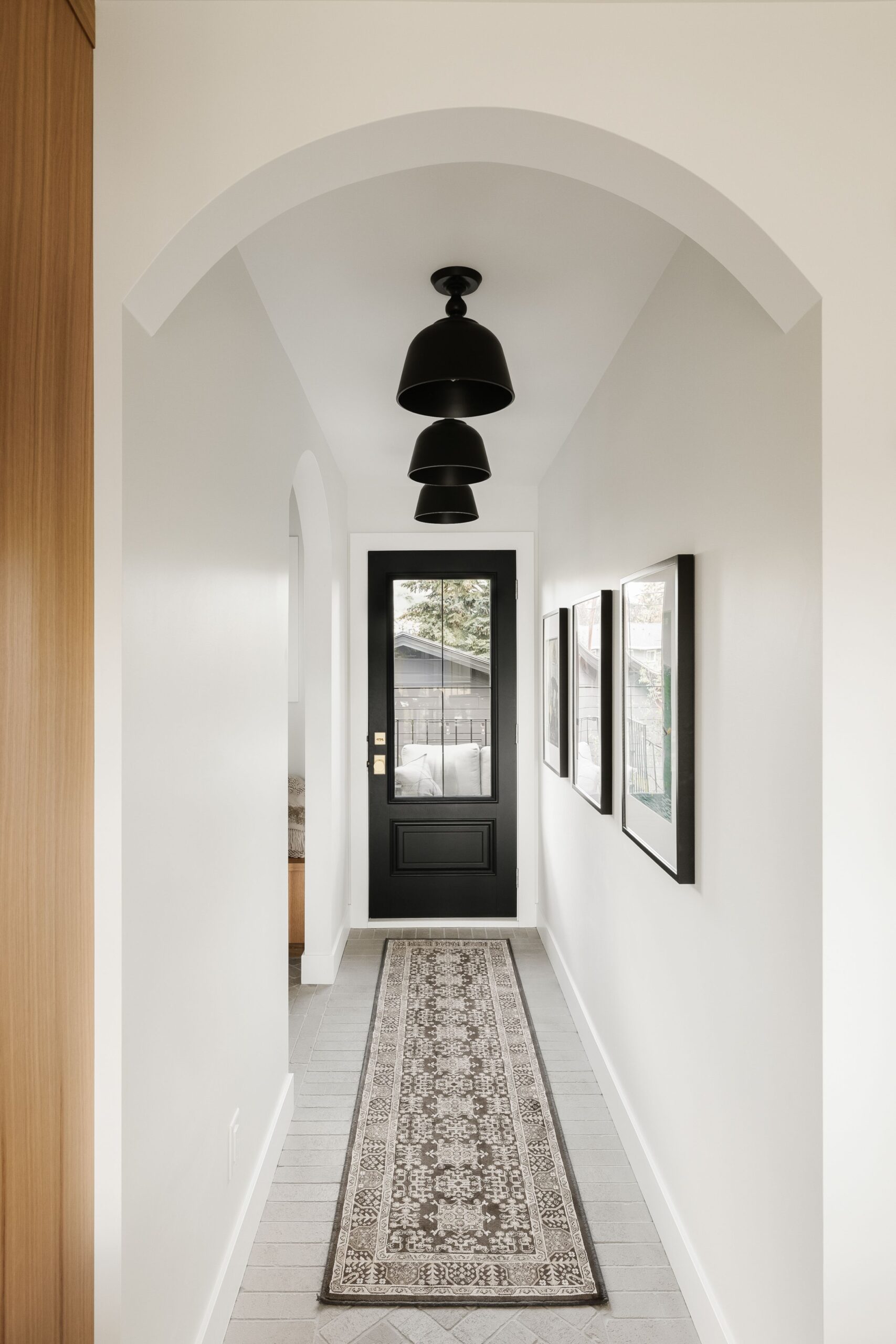 Minimal modern hallway with arched doorway, black door, and layered lighting design by Alderstone Homes, showcasing refined craftsmanship and timeless style.