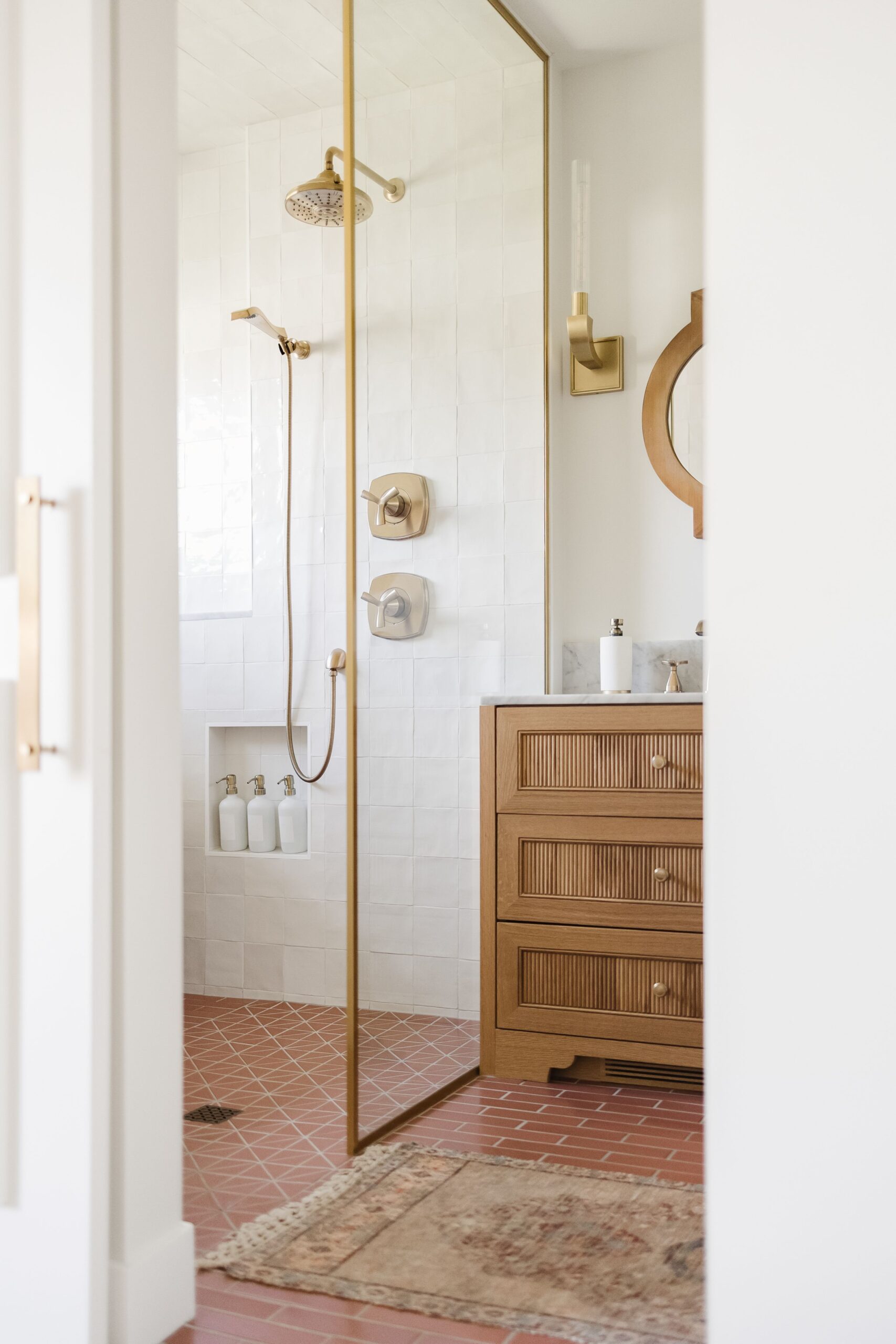 Modern bathroom with white tile shower, brass fixtures, and natural wood vanity designed by Alderstone Homes, blending timeless craftsmanship with contemporary comfort.