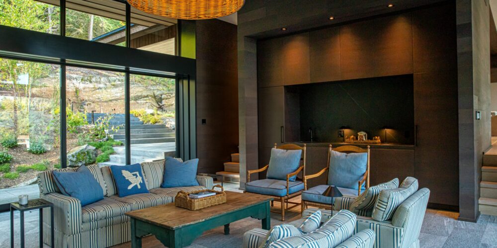 Modern living room with blue seating, woven pendant light, and forest views by Alderstone Homes.